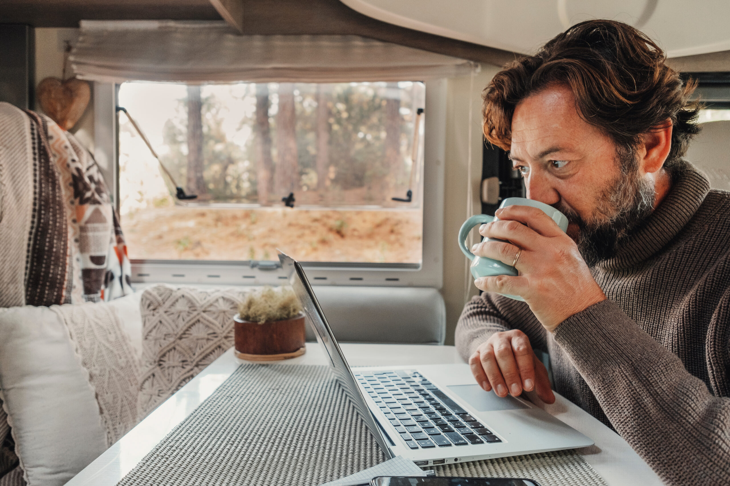 Mature man working on laptop computer inside a camper van with n