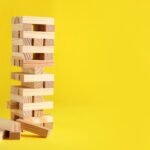 Jenga tower made of wooden blocks on yellow background, space fo