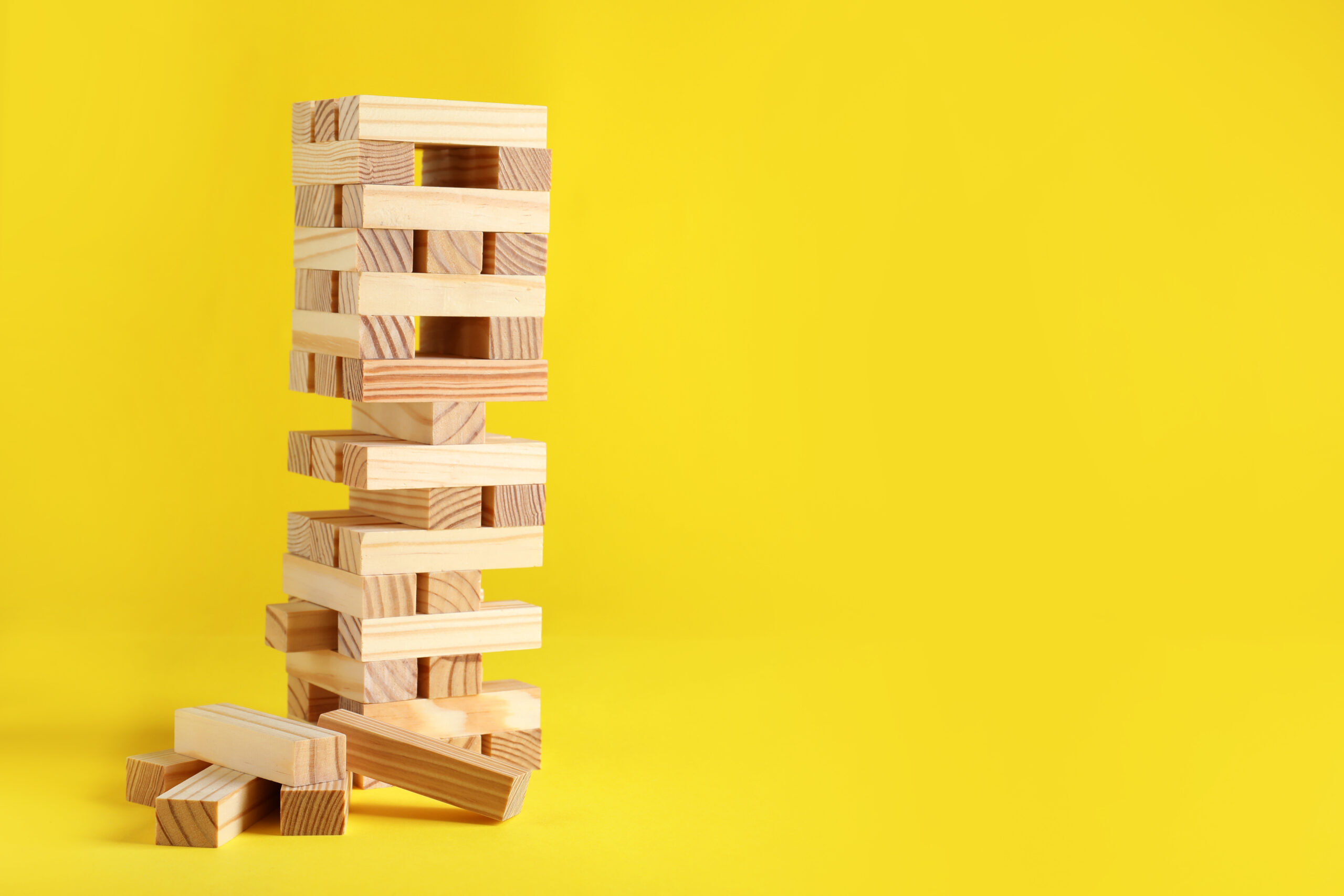Jenga tower made of wooden blocks on yellow background, space fo