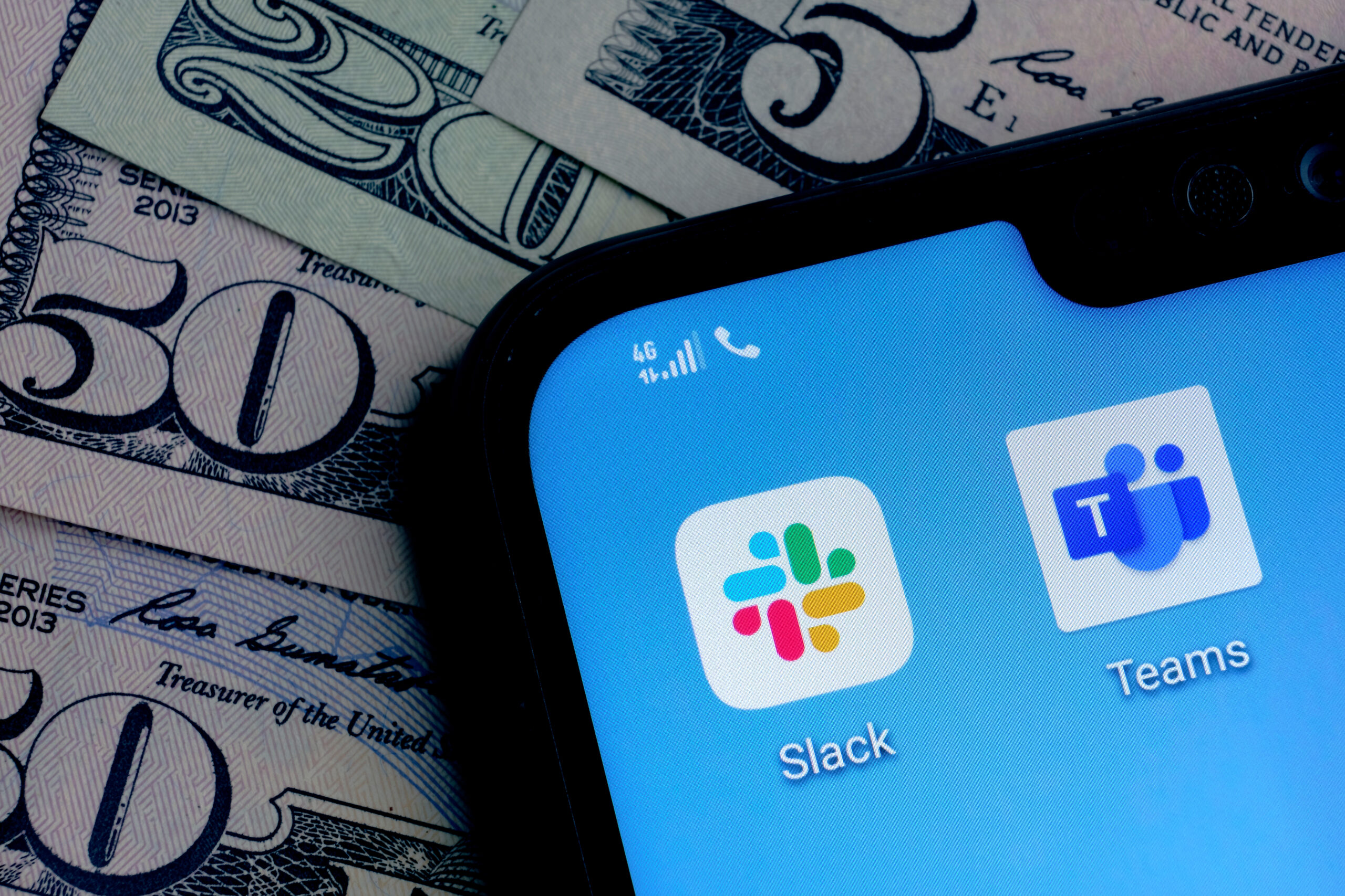 Stone / United Kingdom - July 22 2020: Slack and Microsoft Teams apps on the corner smartphone screen placed on dollar bills background. Concept for competition.