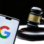 Google logo seen on the smartphone placed next to the judges gavel. Concept for a lawsuit, legal case, antitrust and fine. Real photo, not a montage. Stafford, United Kingdom - December 15 2020.