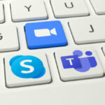 Logos of the competing video conference systems Skype, Zoom and Microsoft Teams (l.t.r.) as keys on a white keyboard.