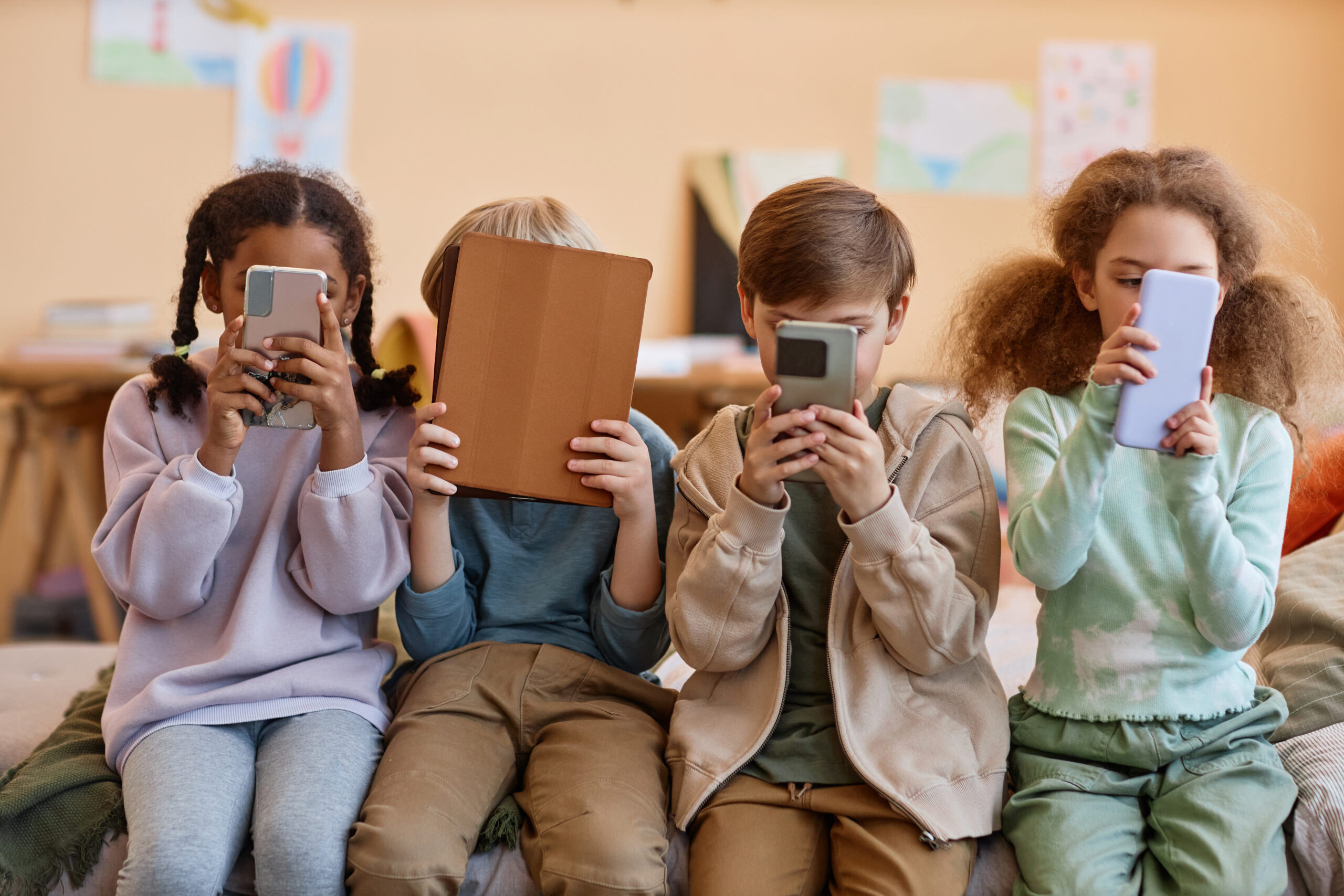 Group of young children holding smartphones and hiding faces