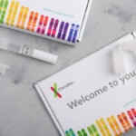 23andMe personal genetic test saliva collection kit, with tube and box on table overhead view.