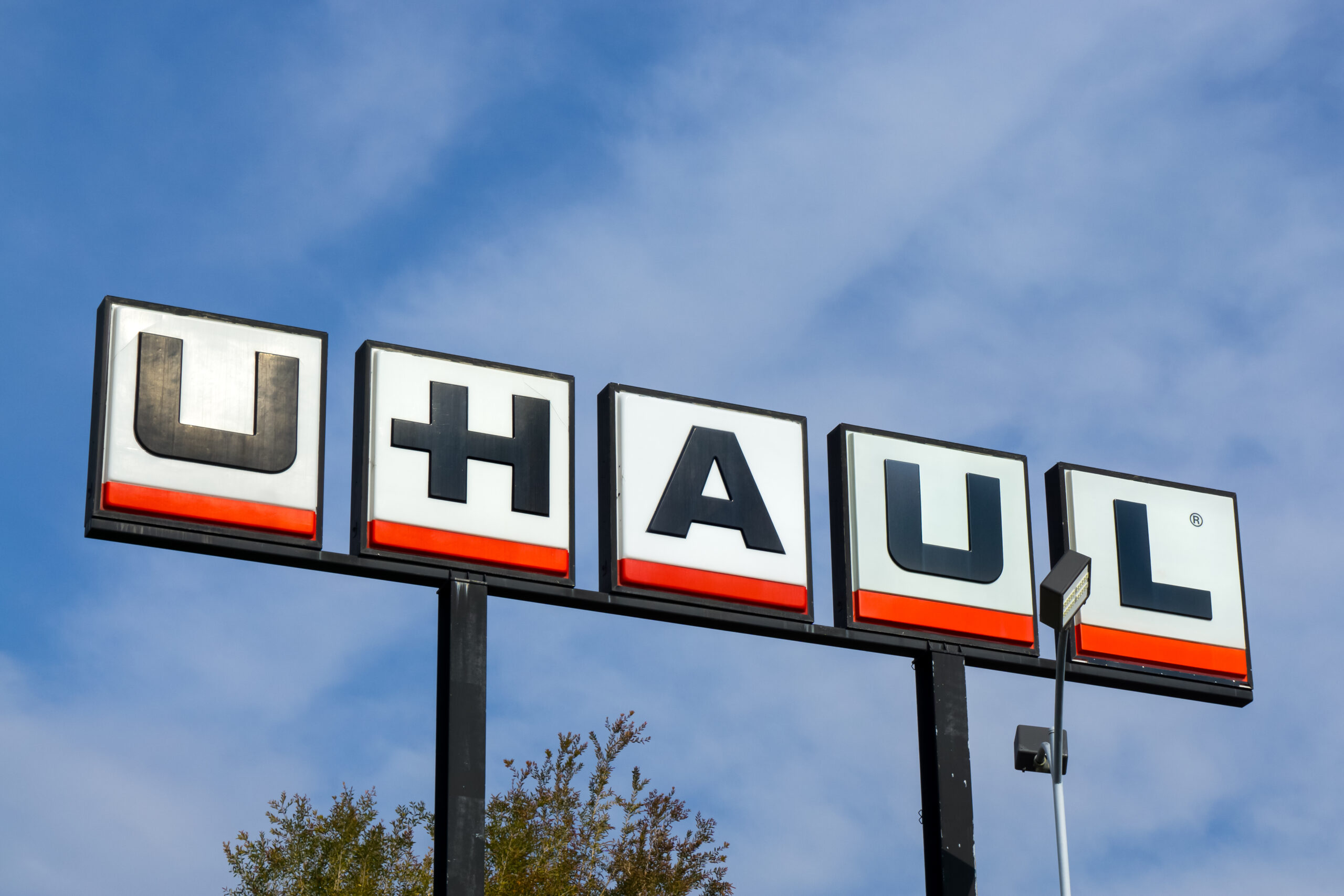 The image displays the signboard of U-Haul, featuring large, bold white letters on a black background with a red underline, against a clear blue sky.