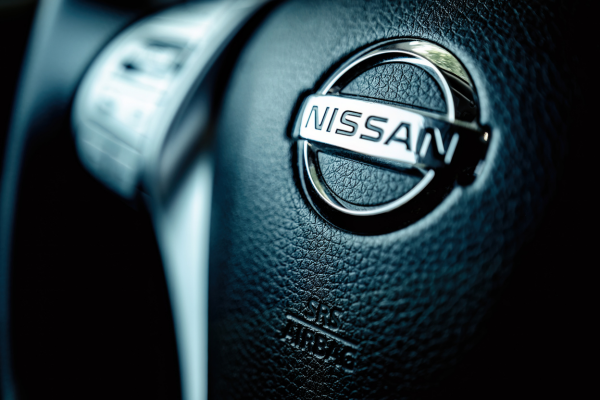 Image of a close-up view of the steering wheel of a Nissan vehicle with a focus on the Nissan emblem in the center.