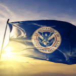 A waving flag with the Department of Homeland Security on it, with the sun shining through the background.