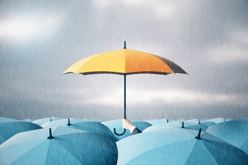 Man hand holding yellow umbrella over crowd on blurry dull sky background. Risk, protection and safety concept.