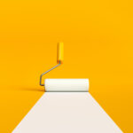 Paint roller brush painting a white line on yellow background. Home improvement, renovation and DIY concepts.