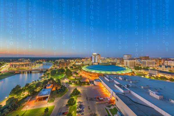 A skyline photo of the city of Wichita with lines of vertical binary code barely visible in the background sky, signifying a cyberattack or hack.