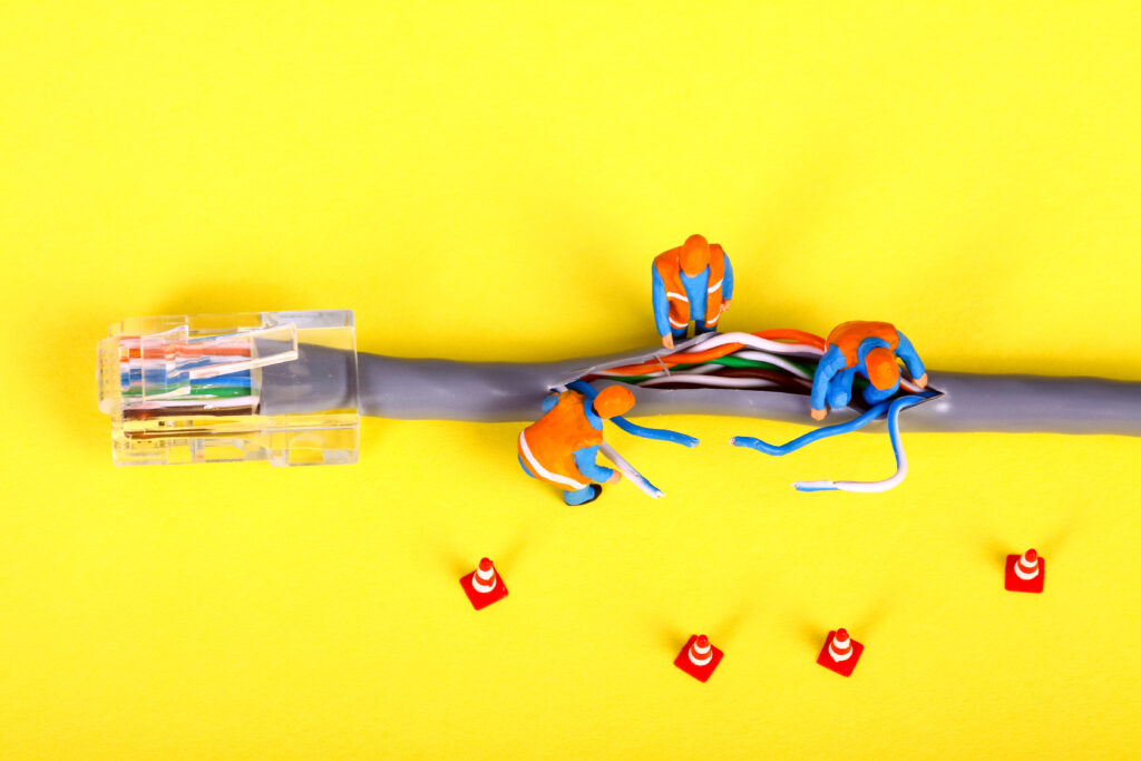 Conceptual image of miniature figure workmen investigating an issue within an internet cable.