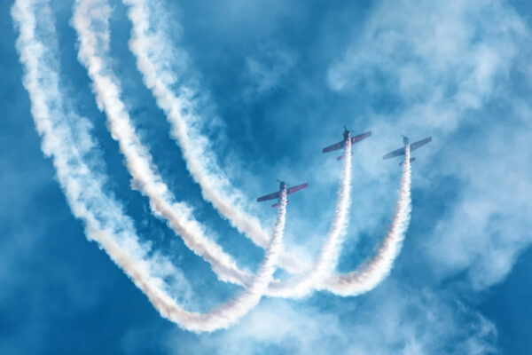 Three light-engine airplane perform aerobatics in a cloud of smoke.