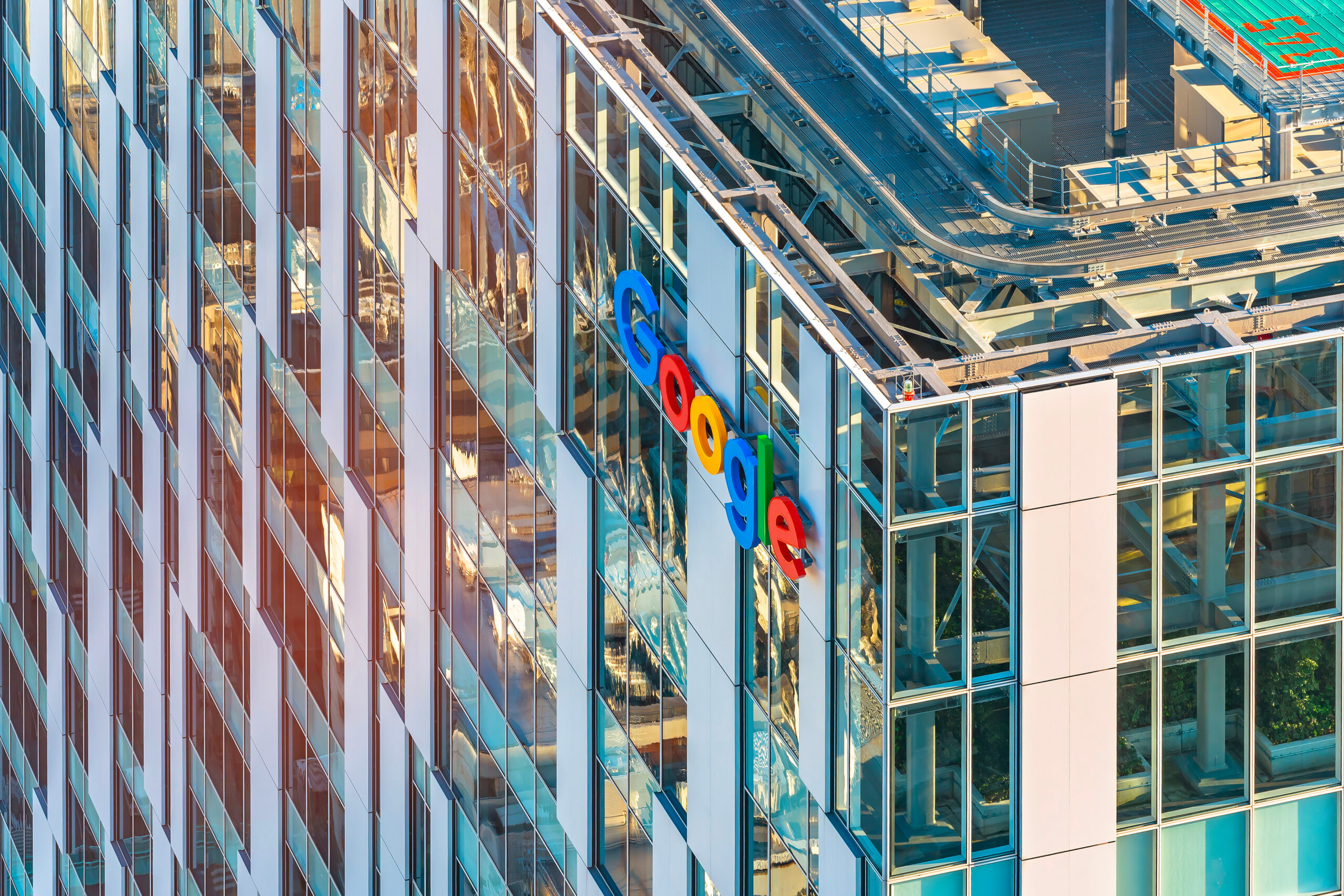 Close up bird’s eye view of a bay window at the corner of the facade of the skyscraper of the internet communications giant Google with its colorful logo on the storefront.