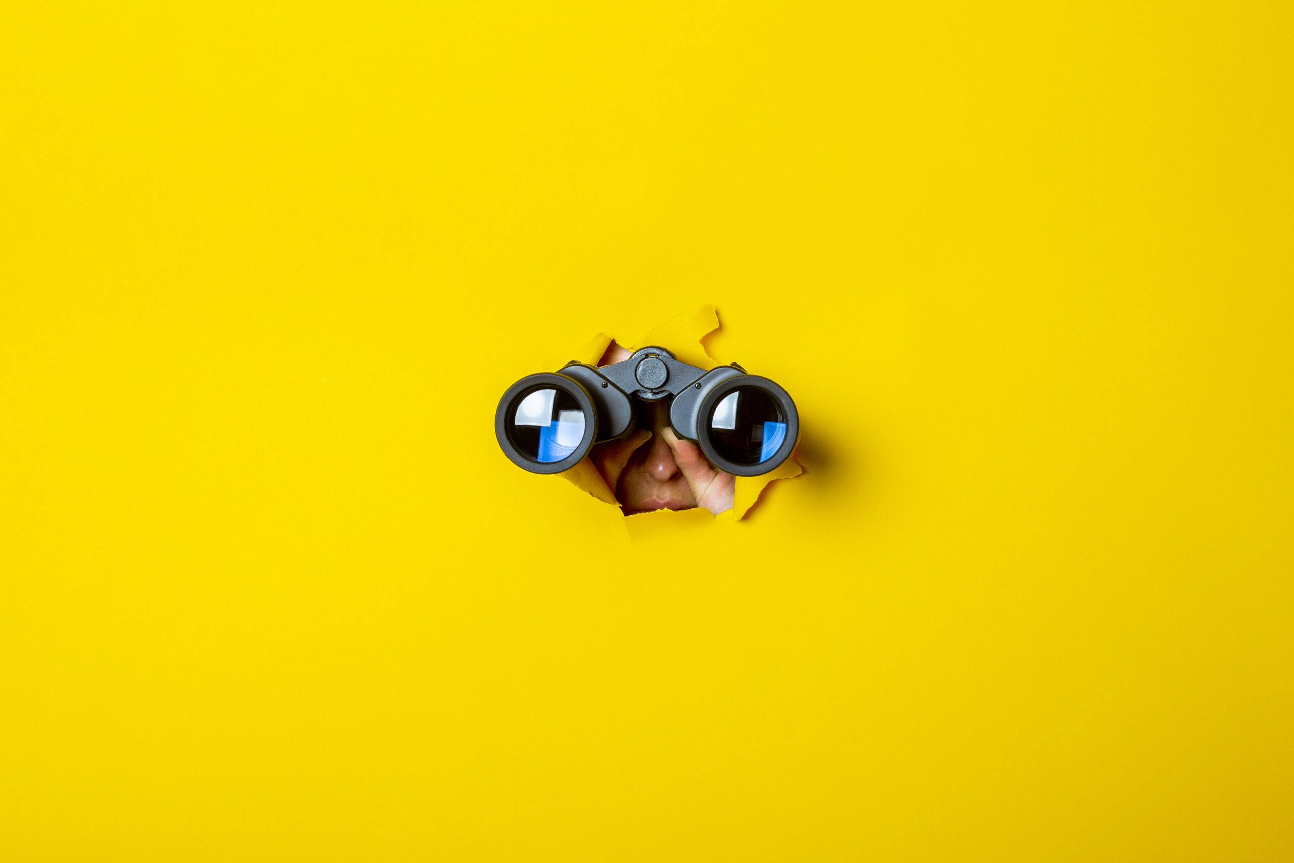 Female hand holds black binoculars on a yellow background. Journey, find and search concept