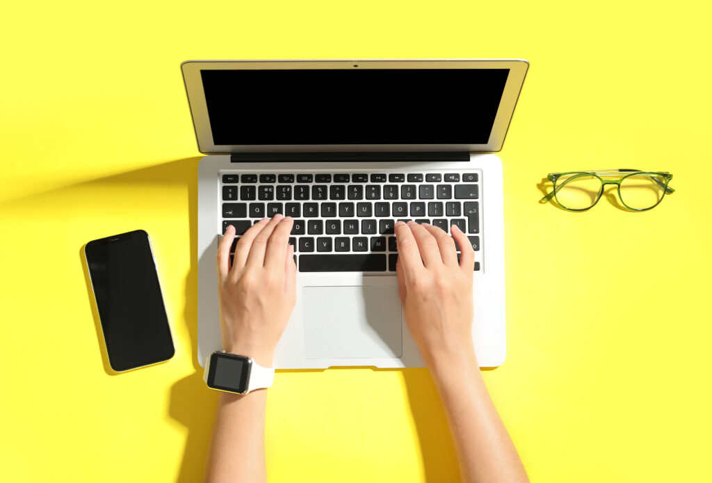 Female hands with laptop, mobile phone and eyeglasses on yellow background