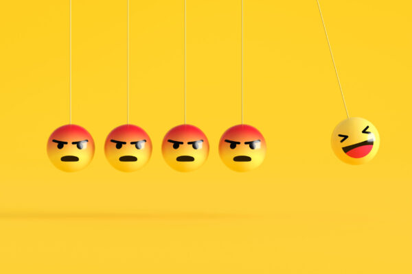 Happy emoji swinging away from angry emojis on yellow background.