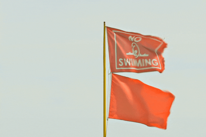 Close up of beach warning flags, the red flag, indicating high hazard/ and or strong currents blows in the breeze with a red "no swimming" flag.