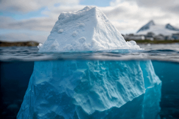A large iceberg floating in clear blue water, showing both its visible tip and massive submerged portion beneath the surface.