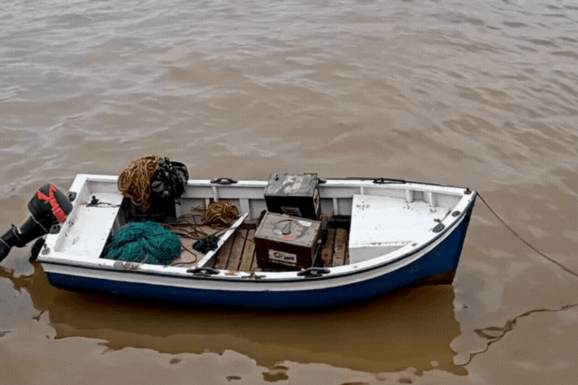 A fishing boat with fishing supplies on it in muddy water.