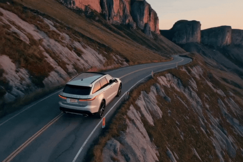 A Jaguar Land Rover driving along a remote, winding mountain road at golden hour.