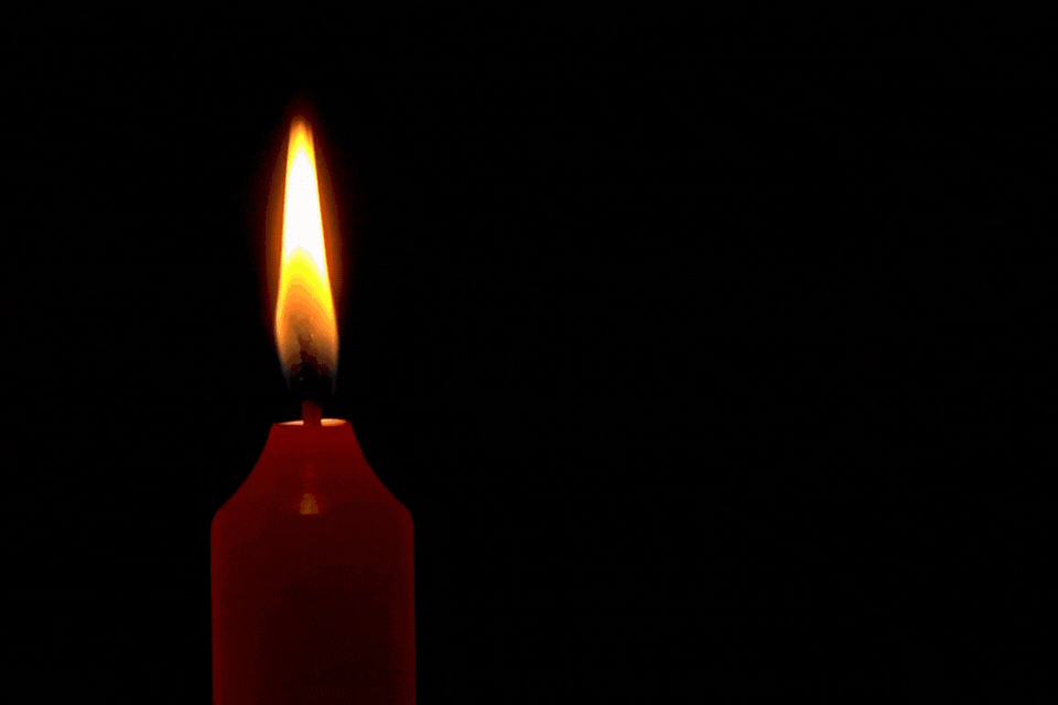 A red candle flame burns in the darkness, slow motion, then is blown out.
