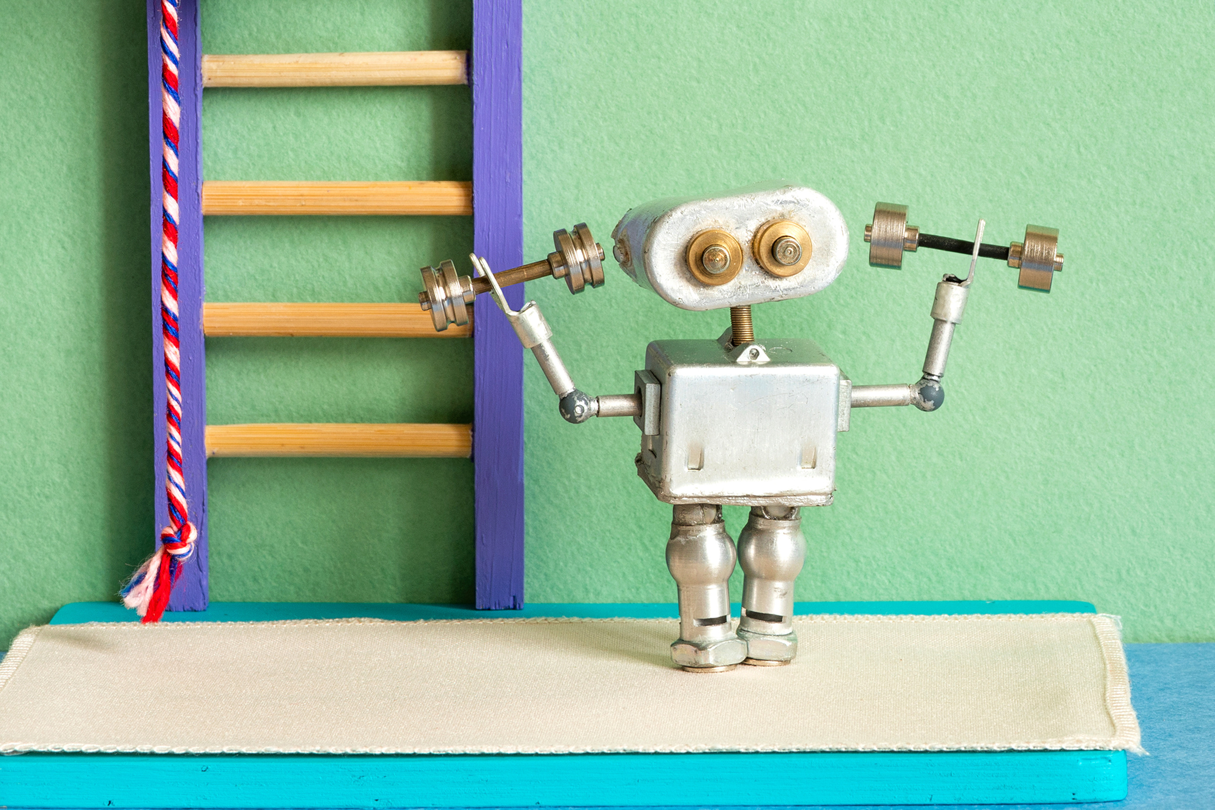 Small silver robot exercising with dumbbells near wall bars. Fitness concept, sports training advertisement