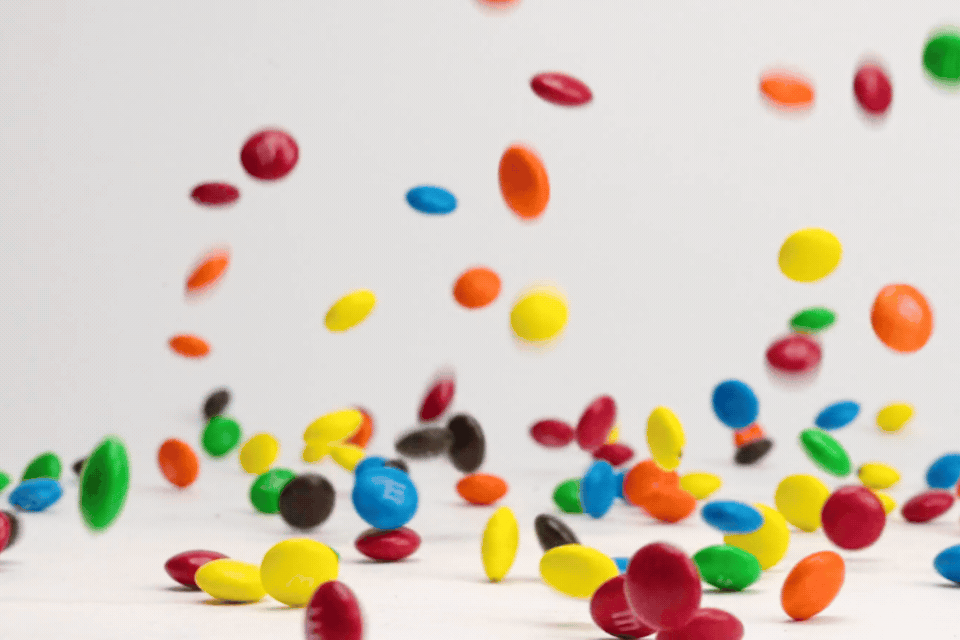 Bright colored chocolate m and m candies bouncing, dancing and spinning on white table top in slow motion