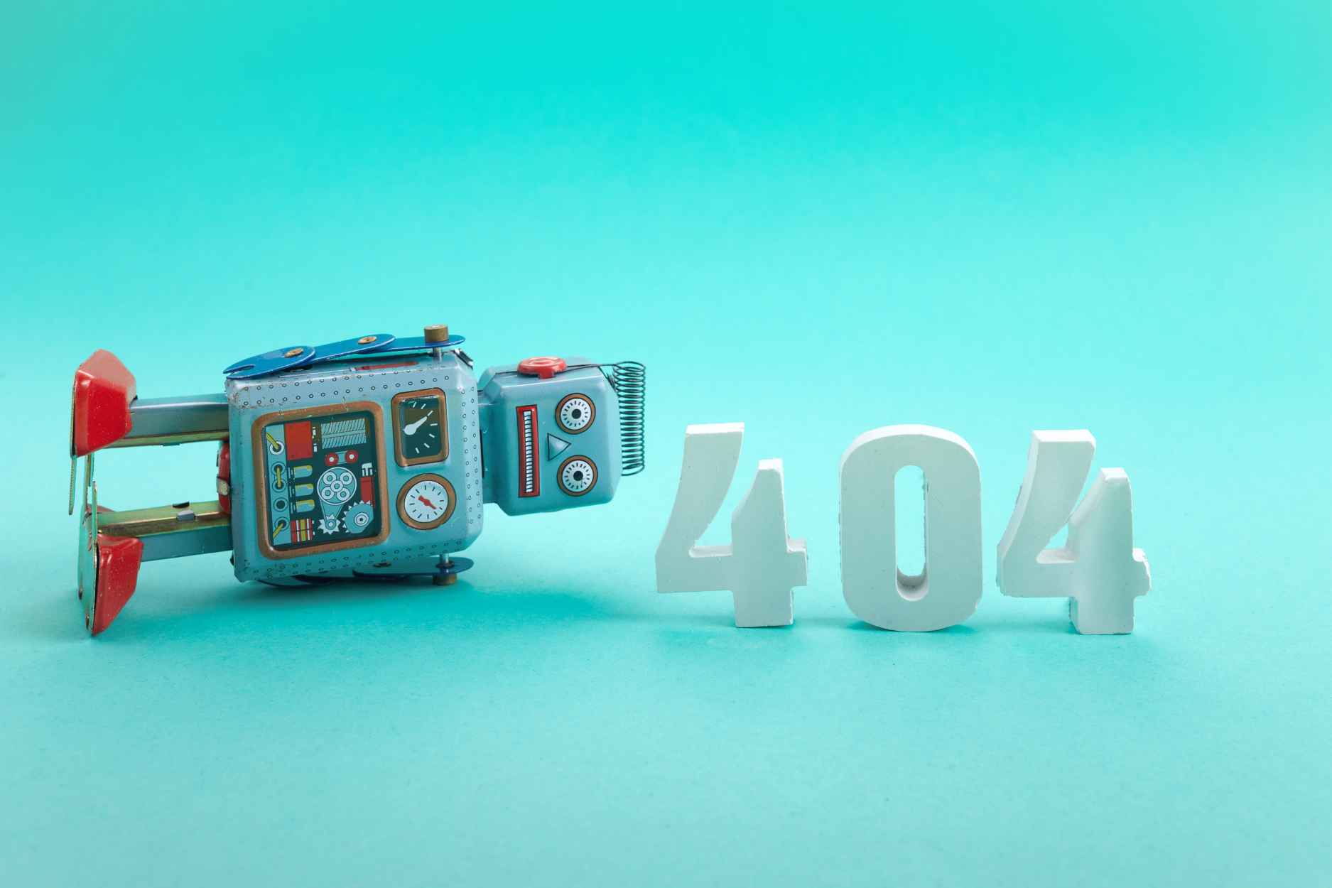A retro toy robot lies beside large white “404” numbers against a bright turquoise background.