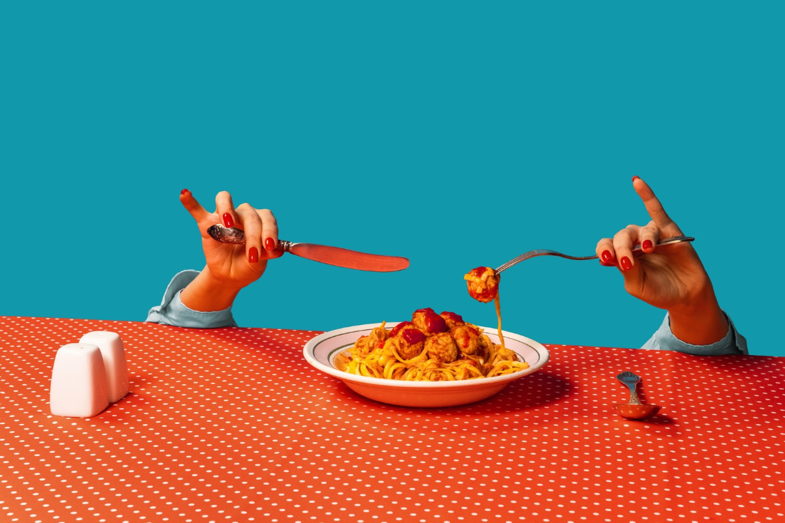 Food pop art photography. Female hands tasting spaghetti with meatballs on plaid tablecloth isolated on bright blue background. Vintage, retro style interior