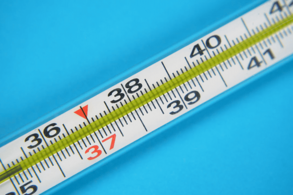 Close-up of a glass thermometer displaying temperatures in Celsius against a bright blue background.